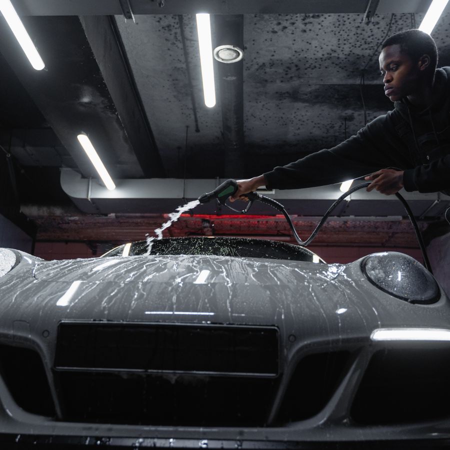 Detailer rinsing a dark sports car under garage lights